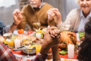 multicultural family holds hands around table and prays before holiday dinner