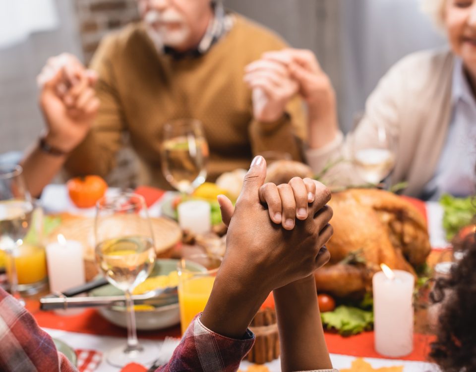 multicultural family holds hands around table and prays before holiday dinner