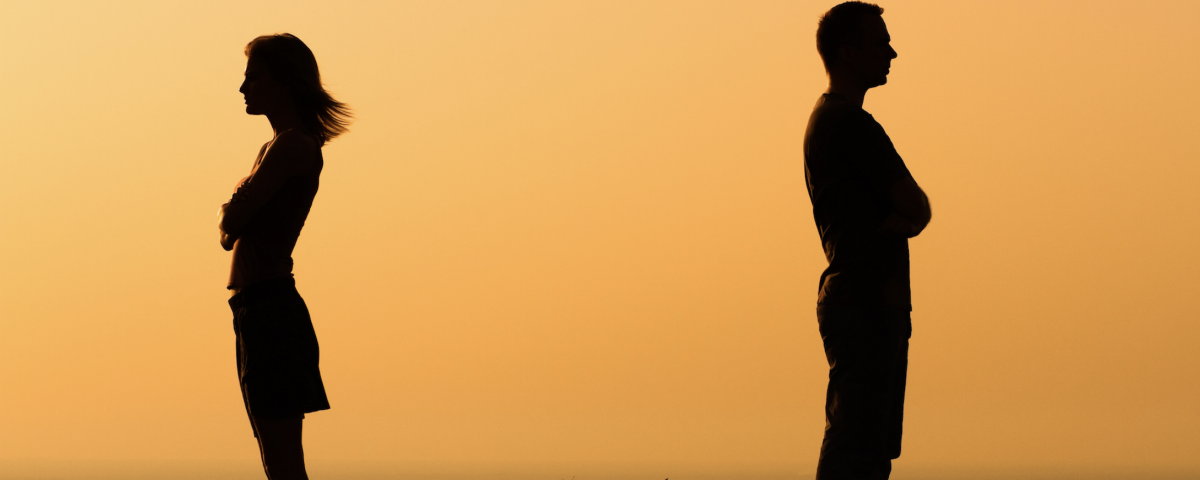 Silhouette of a man and woman with backs to each other crossing their arms with orange sunrise background