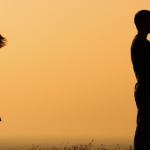 Silhouette of a man and woman with backs to each other crossing their arms with orange sunrise background