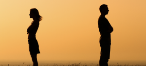 Silhouette of a man and woman with backs to each other crossing their arms with orange sunrise background