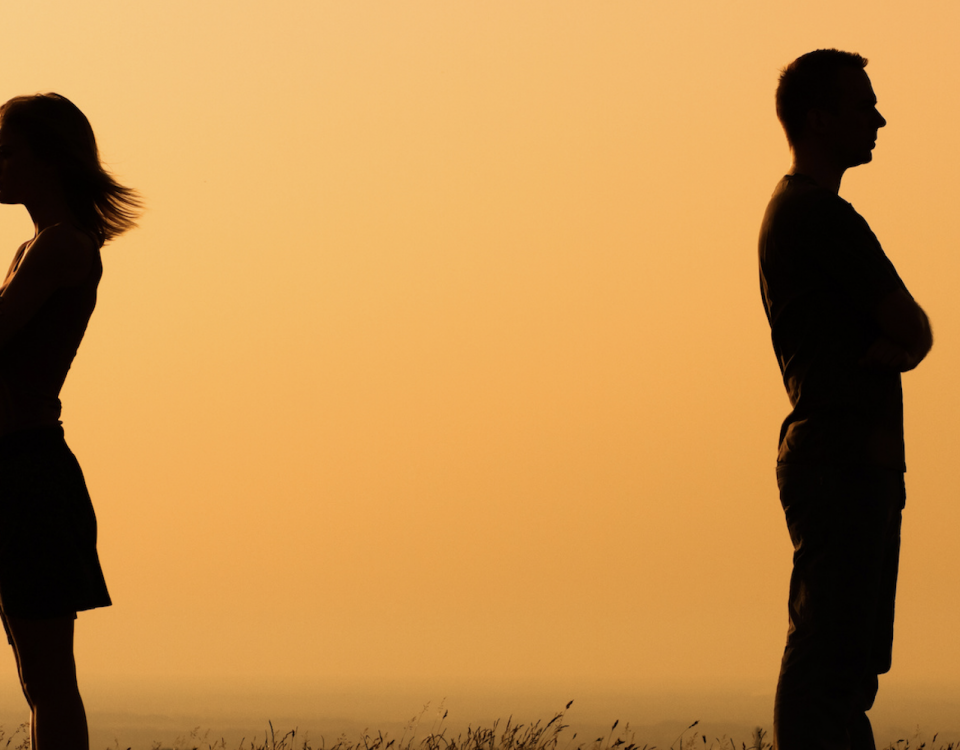 Silhouette of a man and woman with backs to each other crossing their arms with orange sunrise background