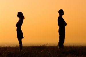 Silhouette of a man and woman with backs to each other crossing their arms with orange sunrise background