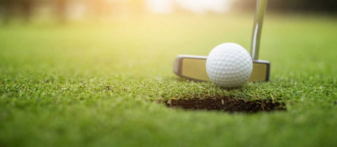 Golfer putting golf ball approach to the golf hole on the green golf