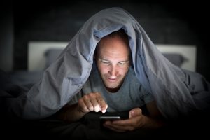 A young cell phone addict man awake late at night in bed using smartphone