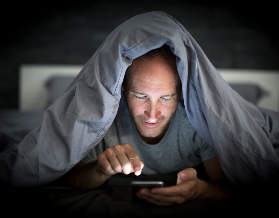 A young cell phone addict man awake late at night in bed using smartphone