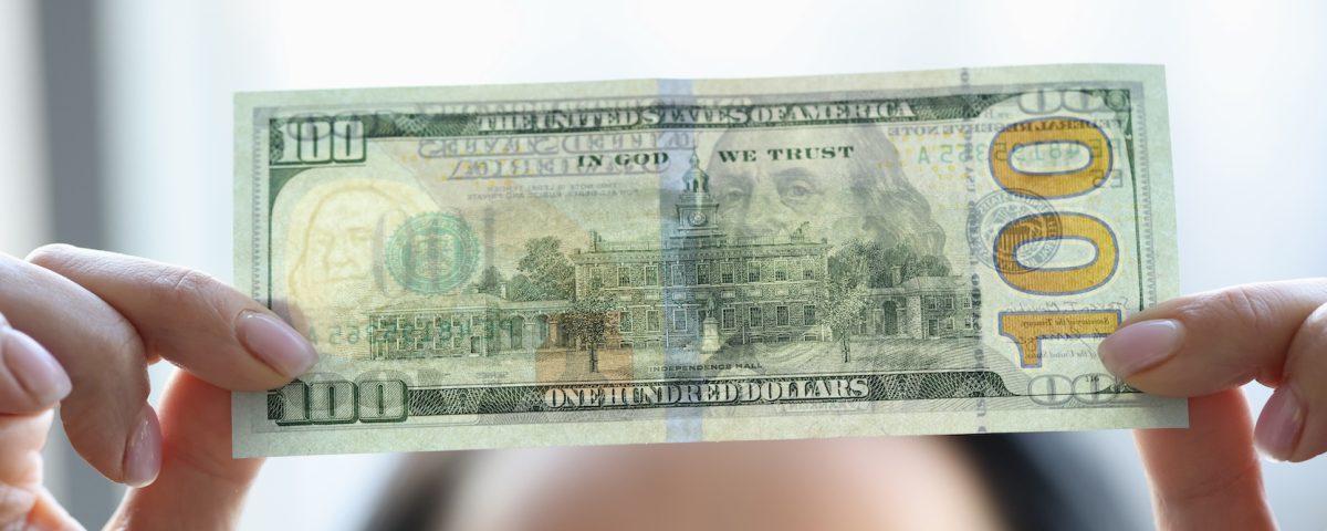Woman holding dollar bill and looking at it with watermarks closeup to see if it's counterfeit.