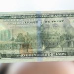 Woman holding dollar bill and looking at it with watermarks closeup to see if it's counterfeit.