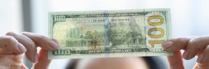 Woman holding dollar bill and looking at it with watermarks closeup to see if it's counterfeit.