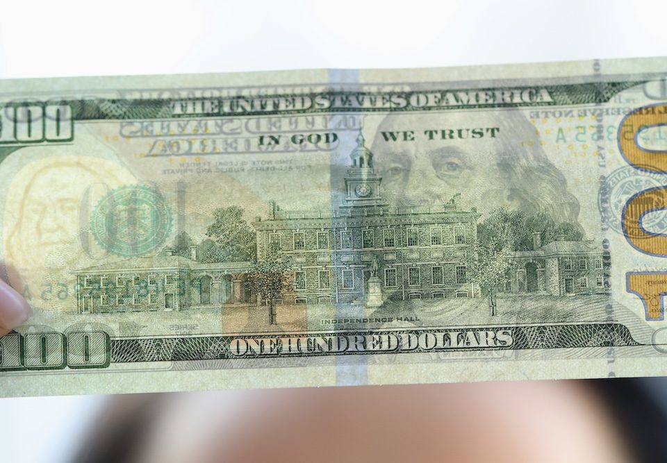 Woman holding dollar bill and looking at it with watermarks closeup to see if it's counterfeit.