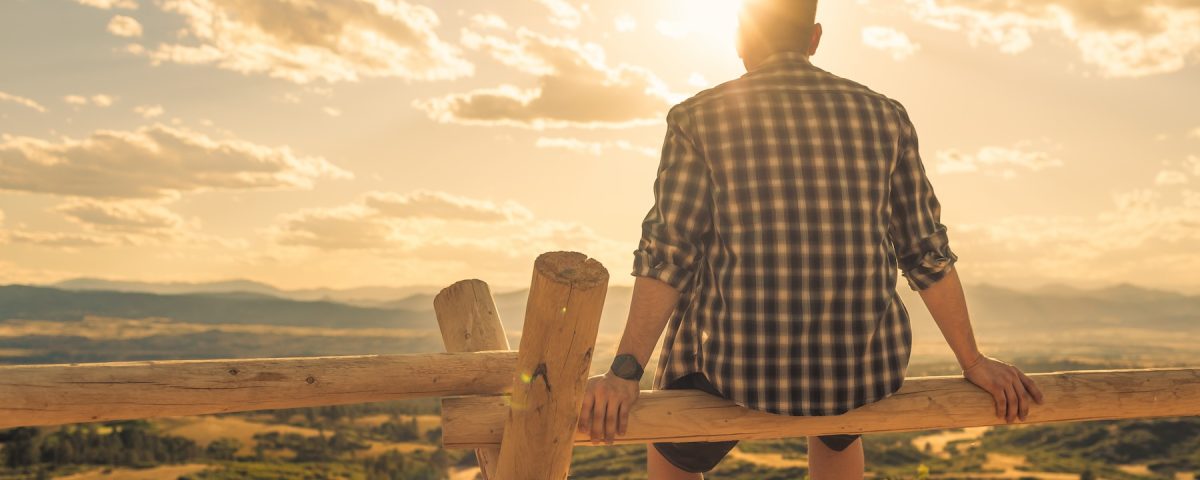 Man sitting on wooden fence and looking at sunrise