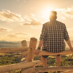 Man sitting on wooden fence and looking at sunrise