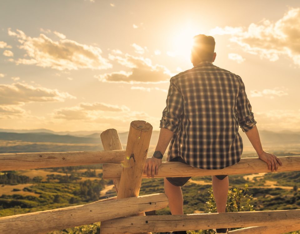 Man sitting on wooden fence and looking at sunrise